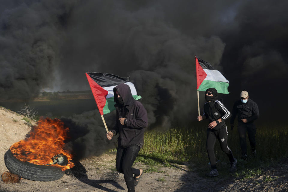 Demonstrators run while wave their national flags as others burning tires during a protest against Israeli military raid in the West Bank city of Nablus, along the border fence with Israel, in east of Gaza City, Wednesday, Feb. 22, 2023. Palestinian officials say several Palestinians have been killed and over a hundred were wounded during a rare daytime Israeli army arrest raid in the occupied West Bank. The Palestinian Health Ministry says a 72-year-old man was among the dead. The raid took place on Wednesday in the city of Nablus, a scene of frequent military activity. (AP Photo/Adel Hana)