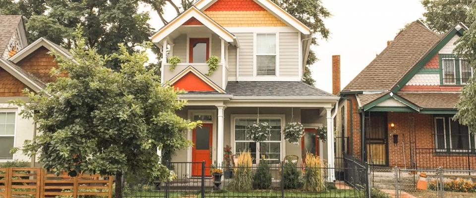 Colorful house on a street with black metal fence outside and red details.