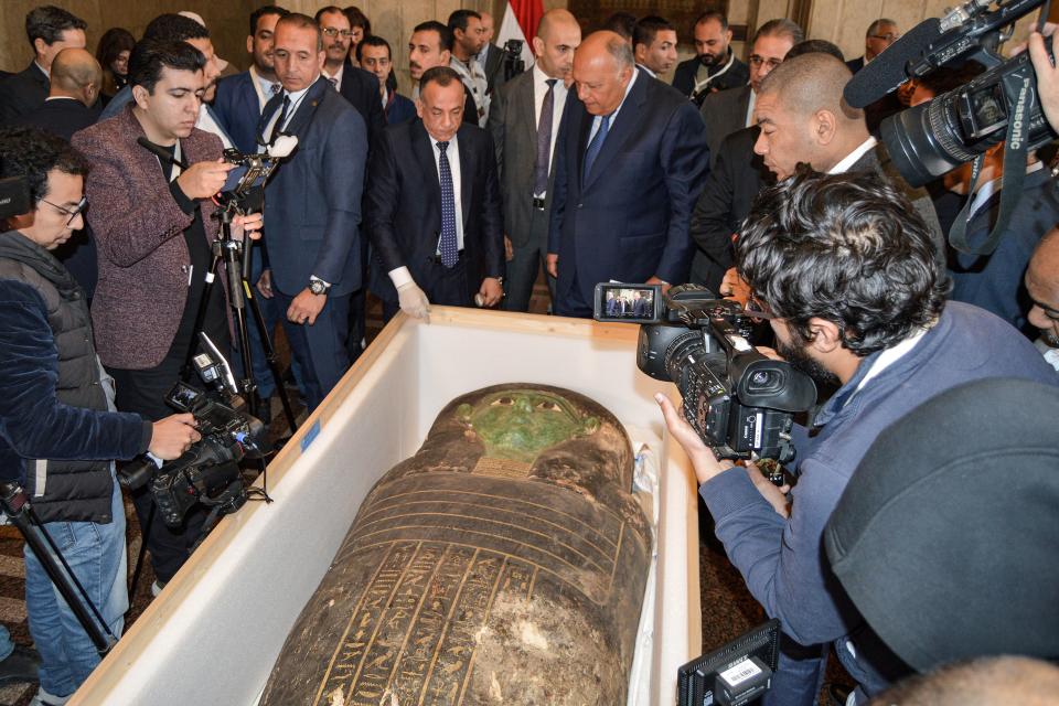 Egypt's Foreign Minister Sameh Shoukry (C-R) and the head of the Supreme Council of Antiquities Mostafa Waziri (C-L) are surrounded by journalists as they inspect an ancient Egyptian wooden sarcophagus being handed over and which was formerly displayed at Houston Museum of Natural Sciences after having been looted and smuggled years prior, at the foreign ministry headquarters in the capital Cairo on January 2, 2023. - Egypt announced on January 2 the recovery of a sarcophagus lid dating back nearly 2,700 years that it said had been smuggled out and put on display at a museum in the United States. Foreign Minister Sameh Shoukry announced the recovery of the artefact, known as the 