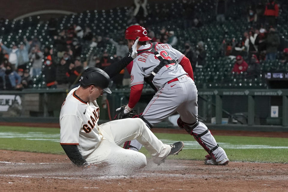 San Francisco Giants' Buster Posey, left, slides home to score past Cincinnati Reds catcher Tucker Barnhart during the sixth inning of a baseball game in San Francisco, Tuesday, April 13, 2021. (AP Photo/Jeff Chiu)