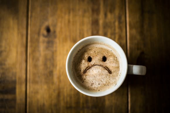 Coffee cup on a brown rustic table, with an unhappy face in the latte art