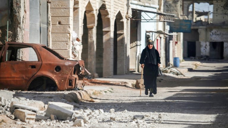 A woman walks with a cane past a destroyed car on a street in Al-Hirak in the eastern Daraa province countryside in southern Syria on June 21, 2018