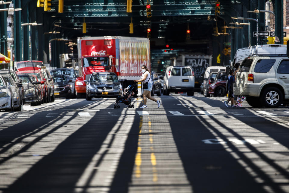 Pedestrians wearing protective face masks pass under elevated train tracks during the COVID-19 pandemic, Tuesday, June 23, 2020, in the Corona neighborhood of the Queens borough of New York. (AP Photo/John Minchillo)