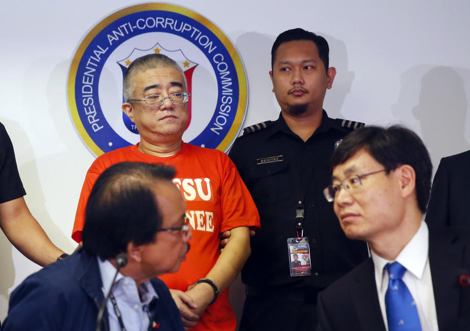 Presidential Anti-Corruption Commission chief Dante Jimenez, seated left, talks to La Yifan, seated right, China's Director for International Cooperation of the Central Commission for Discipline Inspection during a formal turnover for Xie Haojie, standing left, who was arrested in an operation coordinated with Chinese authorities, at a news conference Wednesday, Jan. 16, 2019 in Manila, Philippines. Philippine officials have turned over to China the former government official wanted for alleged economic crime and corruption. (AP Photo/Bullit Marquez)