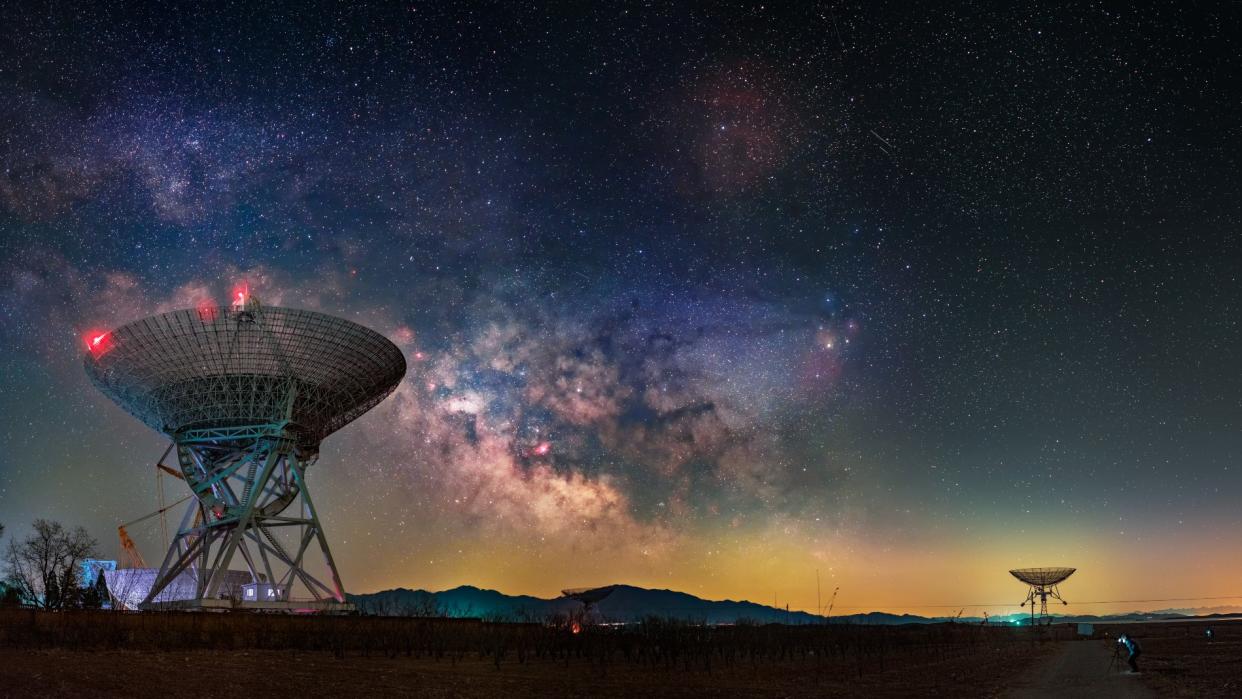  An image of two radio telescope dishes beneath a sky of swirling stars  