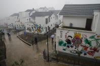 People walk by new village houses decorated with colourful paintings built by the Chinese government for ethnic minority members in Ganluo county, southwest China's Sichuan province on Sept. 10, 2020. The ruling Communist Party says its initiatives have helped to lift millions of people out of poverty. Yi ethnic minority members were moved out of their mountain villages in China’s southwest and into the newly built town in an anti-poverty initiative. (AP Photo/Andy Wong)