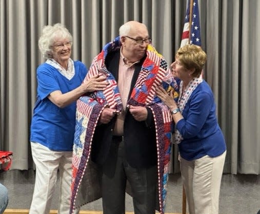 Quilters Joanne Shafer (at left) and Didi Salvatierra wrap veteran Mike Butrum in his Quilt of Valor.