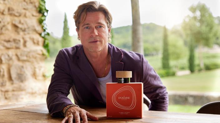 Brad Pitt launches his skincare line, pictured wearing a purple T-shirt and a large red box of his new product