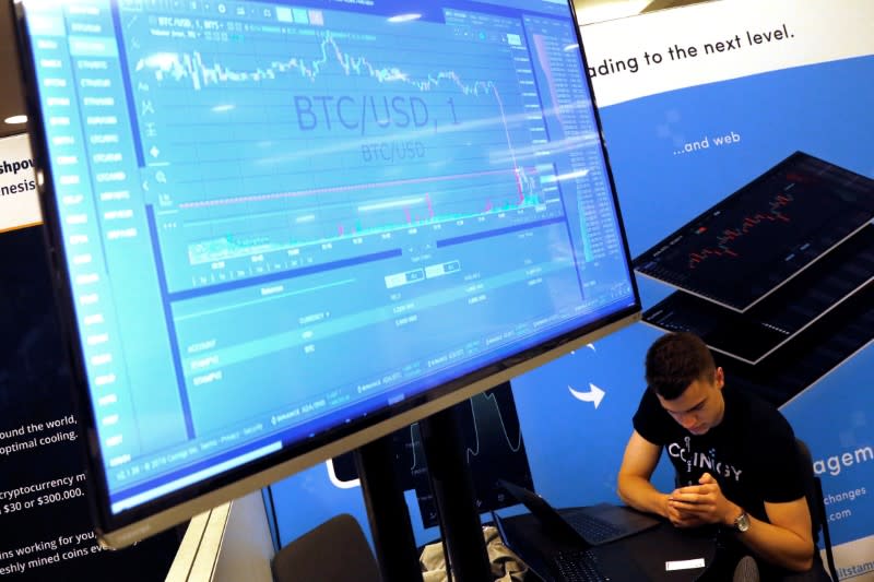FILE PHOTO: A man works beneath a display showing the market price of Bitcoin on the floor of the Consensus 2018 blockchain technology conference in New York City