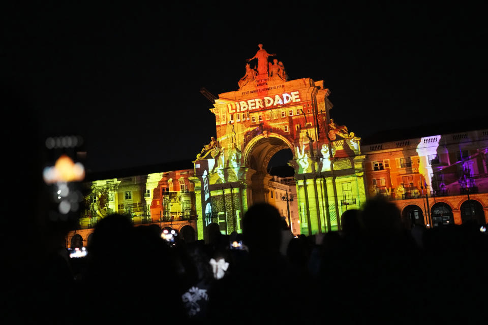 People use their cellphones to take pictures of a light show projecting the word Freedom on the arch of Lisbon's Comercio square, Wednesday, April 23, 2024, as the country celebrates the fiftieth anniversary of the Carnation Revolution. The April 25, 1974 revolution carried out by the army restored democracy in Portugal after 48 years of a fascist dictatorship. (AP Photo/Armando Franca)