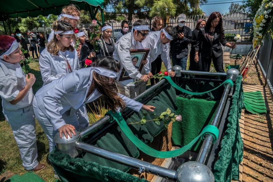 Trang Nguyen, left, throws a rose as the casket is lowered at the funeral of her father-in-law Dung Tan Nguyen on Wednesday, May 6, 2020, during the coronavirus outbreak. Immediate family members, dressed in white, were permitted to approach as a group after the casket was lowered into the grave. All other mourners had to come up in pairs due to social distancing restrictions.