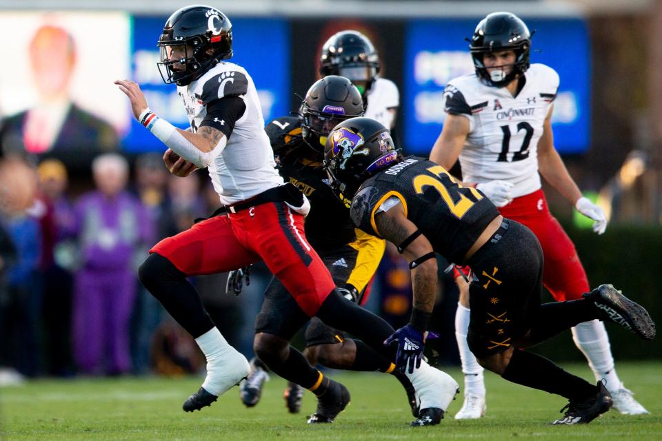 Cincinnati Bearcats quarterback Desmond Ridder (9) runs downfield as East Carolina Pirates safety Juan Powell (7) and East Carolina Pirates safety Shawn Dourseau (27) miss a tackle opportunity in the first half of the NCAA football game between the Cincinnati Bearcats and the East Carolina Pirates at Dowdy-Ficklen Stadium in Greenville, NC, on Friday, Nov. 26, 2021.