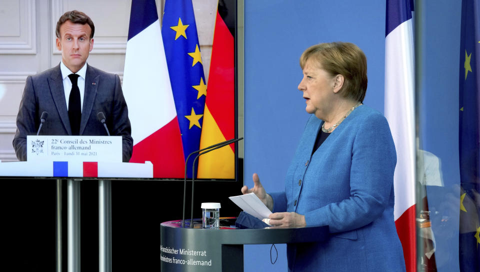 French President Emmanuel Macron is seen on a video screen during a joint press conference with German Chancellor Angela Merkel, right, as part of a virtual Plenary Session of the Franco-German Council of Ministers in Berlin, Germany, Monday, May 31, 2021. (AP Photo/Michael Sohn, pool)