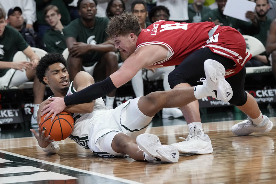 Wisconsin guard Max Klesmit (11) reaches in on Michigan State guard Jaden Akins (3) as they chase the loose ball during the first half of an NCAA college basketball game, Tuesday, Dec. 5, 2023, in East Lansing, Mich. (AP Photo/Carlos Osorio)