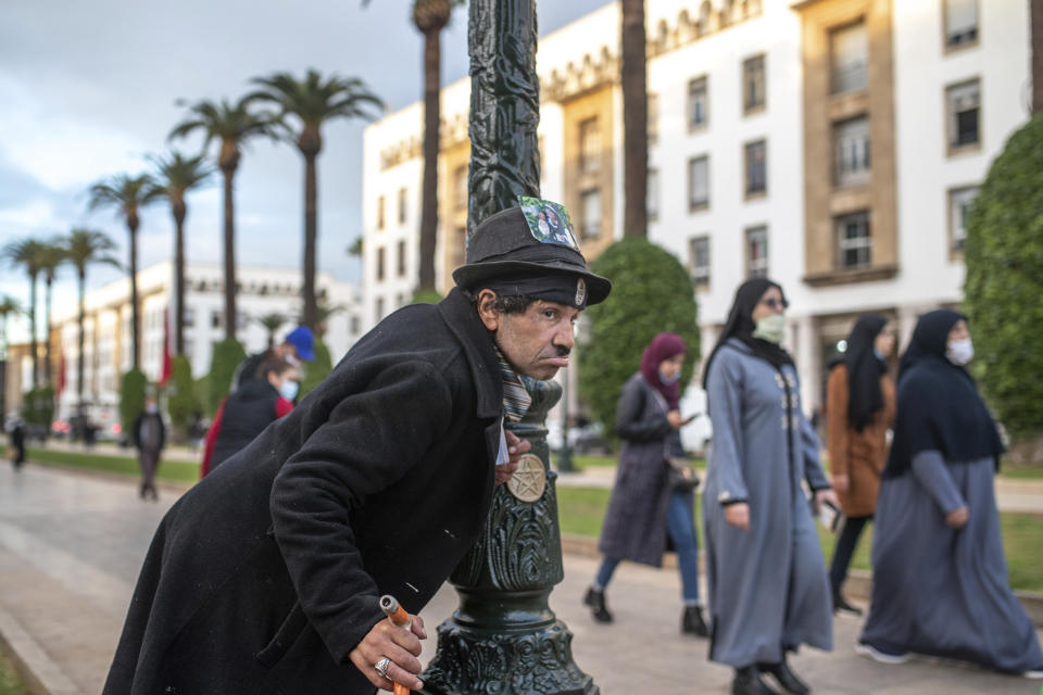 Belhussein Abdelsalam, a Charlie Chaplin impersonator performs as people walk past in an avenue in Rabat, Morocco, Thursday, Dec. 17, 2020. When 58-year-old Moroccan Belhussein Abdelsalam was arrested and lost his job three decades ago, he saw Charlie Chaplin on television and in that moment decided upon a new career: impersonating the British actor and silent movie maker remembered for his Little Tramp character. (AP Photo/Mosa'ab Elshamy)