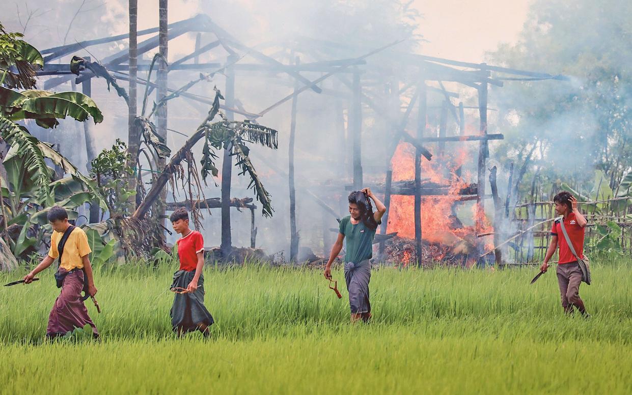 Unidentified men carrying knives and slingshots walk past a burning village near Maungdaw in Rakhine state, on 7 September, 2017. Many Rohingya have died trying to flee the fighting, not making it to the refugee camps in Bangladesh - This content is subject to copyr