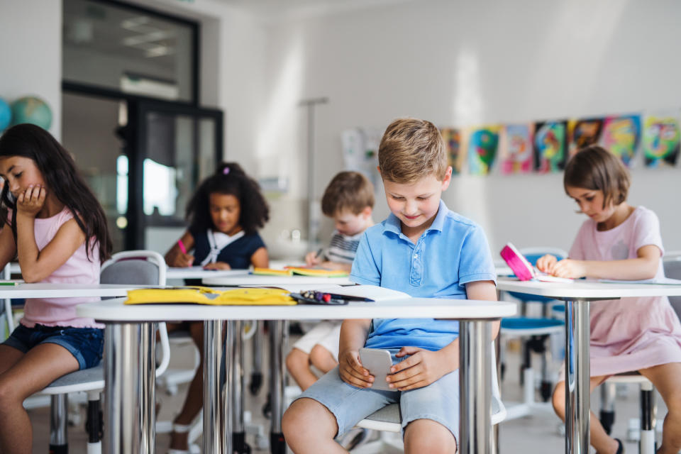 An occupied small school boy with smartphone sitting at the desk in classroom