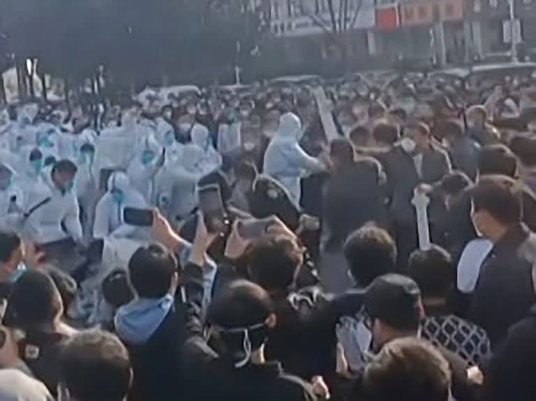 Esta imagen tomada de un vídeo de AFP y publicada el 23 de noviembre de 2022 muestra a los trabajadores de la fábrica de iPhone de Foxconn en Zhengzhou, en el centro de China, enfrentándose a la policía antidisturbios y a personas con trajes de protección. 