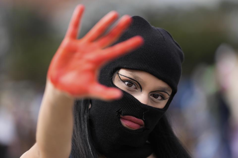 Una mujer enmascarada muestra la palma teñida de rojo de su mano durante la marcha del Día Internacional de la Mujer en Bogotá, Colombia, el miércoles 8 de marzo 2023. (AP Foto/Fernando Vergara)