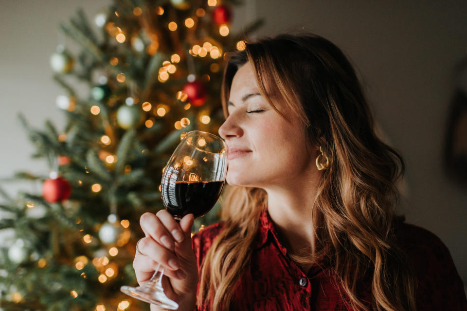 Woman smelling glass of wine beside decorated Christmas tree