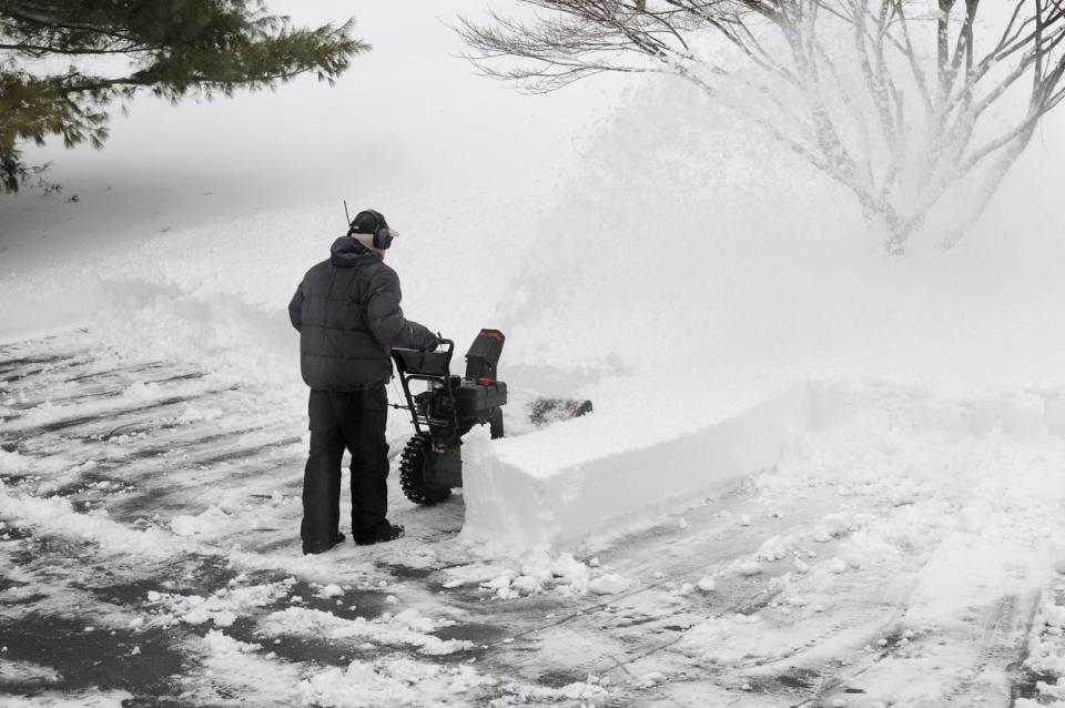 Man snow blowing rows of snow in driveway. 