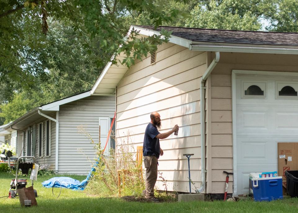 Having previously used a power washer, Mike Gedeon applies white primer paint to cover graffiti painted on the side and garage door of his Green Oak Township home Wednesday, Aug. 11, 2021.