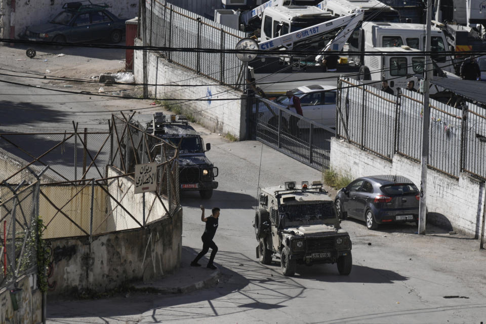 A Palestinian man throws stones at a convoy of Israeli military vehicles, during a raid in the West Bank city of Nablus, Thursday, May 4, 2023. The Israeli military says it has killed three Palestinians wanted for an attack last month on a car near a Jewish West Bank settlement that killed a British-Israeli mother and two of her daughters. The military says a fierce gunbattle erupted when the army entered the heart of the flashpoint city of Nablus early Thursday. (AP Photo/Majdi Mohammed)