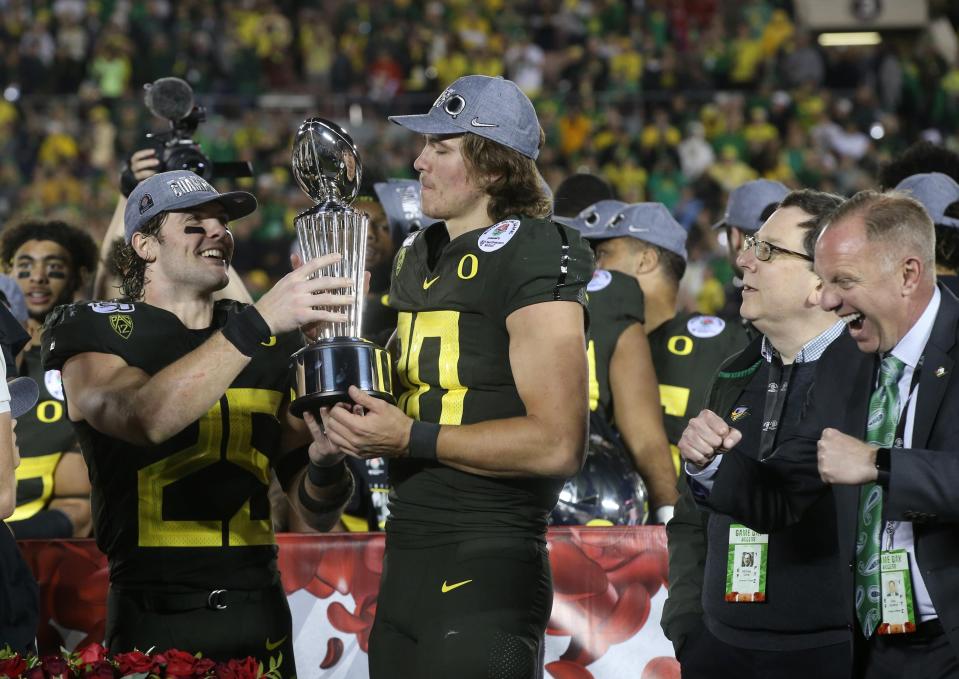 Oregon's Brady Breeze (25) hands the Rose Bowl trophy to Justin Herbert as they celebrate the Ducks' 28-27 win over Wisconsin on Jan. 1, 2020, as school President Michael Schill, second from right, and athletic director Rob Mullens, right, look on.