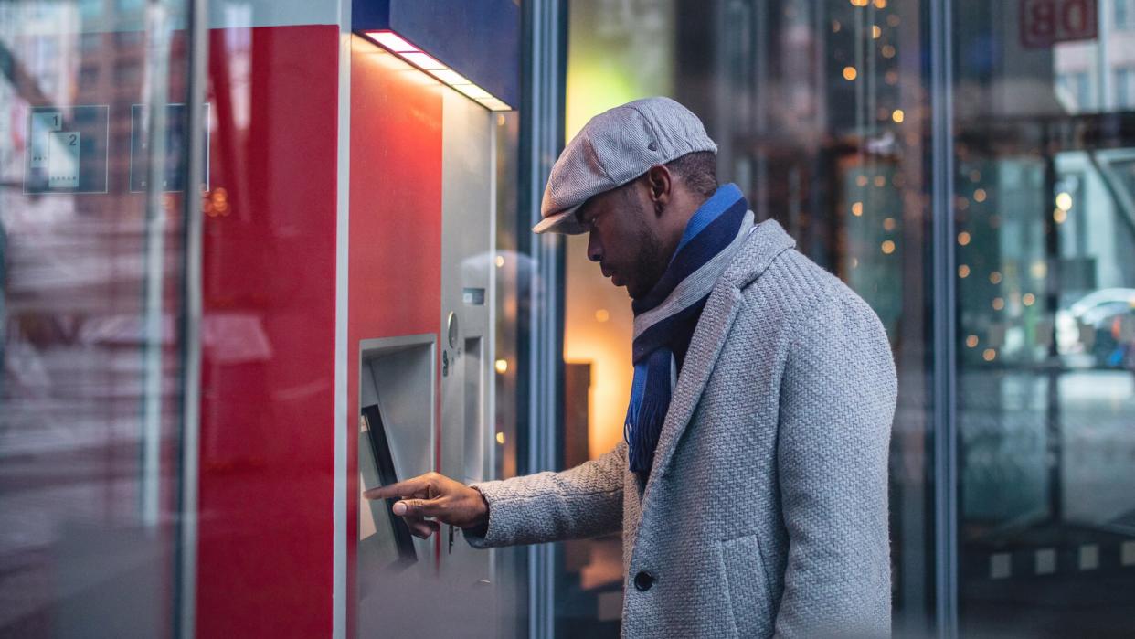 Handsome and beautiful black businessman using a ATM machine in the city.