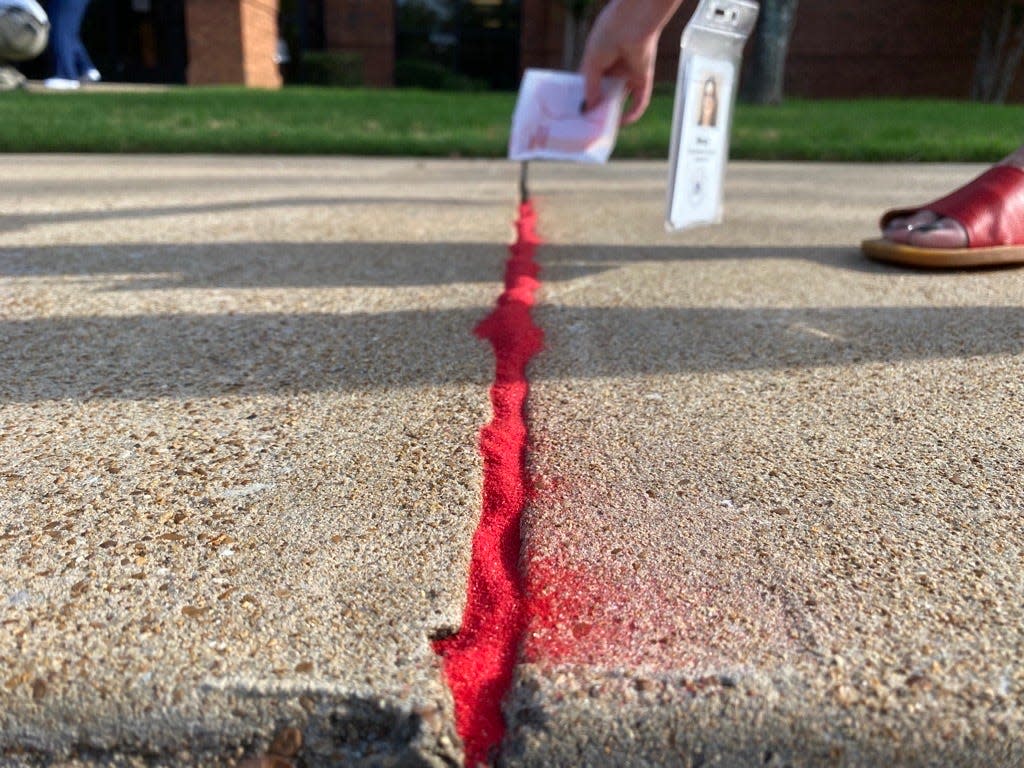 Members of the Jackson-Madison County Regional Health Department poured red sand into the cracks of the department's sidewalks to draw attention to the victims that “fall through the cracks” of society.