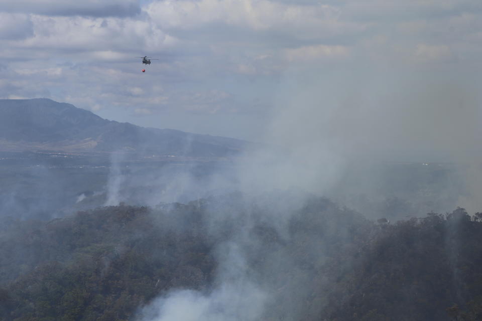 This photo provided by the Hawaii Department of Land and Natural Resources shows an Army helicopter carrying water to douse a wildfire burning east of Mililani, Hawaii, on Thursday, Nov. 2, 2023. A wildfire that has burned forestlands in a remote mountainous area of Central Oahu has moved eastward and away from population centers as firefighters continued to battle the blaze. (Dan Dennison/Hawaii Department of Land and Natural Resources via AP)