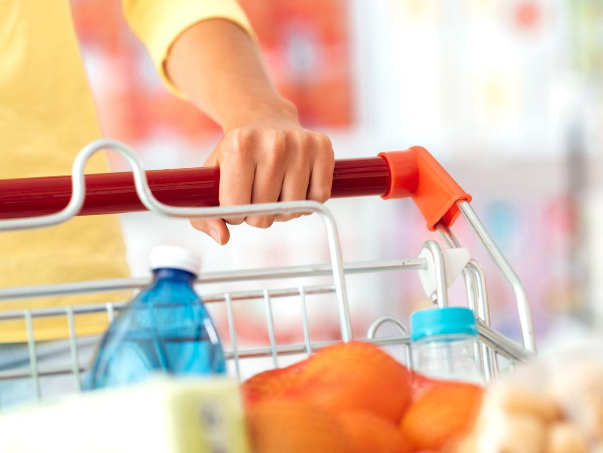 Woman doing grocery shopping at the supermarket and pushing a full shopping cart, hand detail close up, lifestyle concept