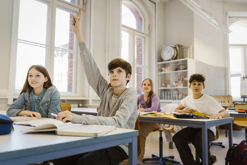 Students in class, one raising hand to answer, indicating active participation and eagerness to learn