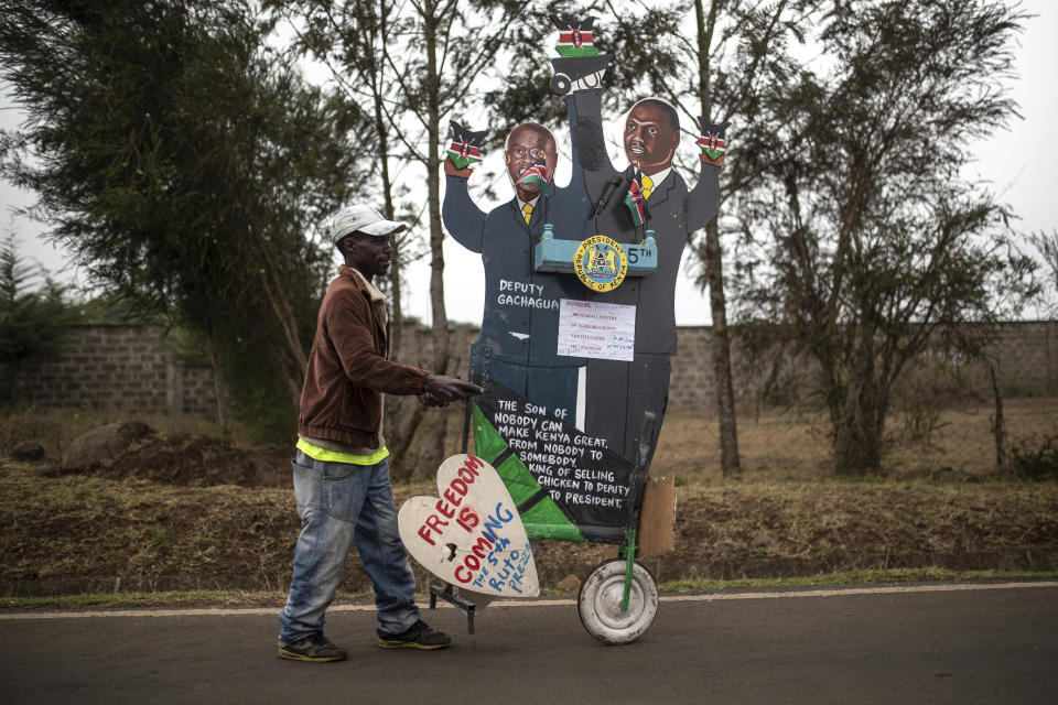 A supporter of Kenya's President-elect William Ruto pushes a cart with cardboard cutout of the president and his running mate, outside the official residence of the deputy president in the Karen area of Nairobi, Kenya Wednesday, Aug. 17, 2022. (AP Photo/Mosa'ab Elshamy)