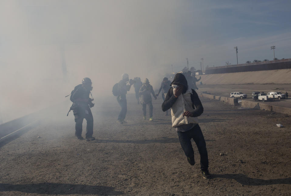 FILE - In this Nov. 25, 2018, file photo, migrants run from tear gas launched by U.S. agents, amid photojournalists covering the Mexico-U.S. border, after a group of migrants got past Mexican police at the Chaparral crossing in Tijuana, Mexico. Children torn from their parents, refugees turned away, tear gas fired on asylum-seekers, and a swath of the globe derided by the president in crude language. In a breathless 2018, they were just a handful of headlines on immigration, one of the year’s most dominant issues. (AP Photo/Rodrigo Abd, File)