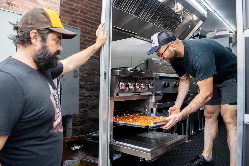 Nathan Drysdale puts a tray of sweet potatoes in an oven as Taco Billy owner, Hunter Berry, looks on at the Little Billy food truck May 15, 2023.