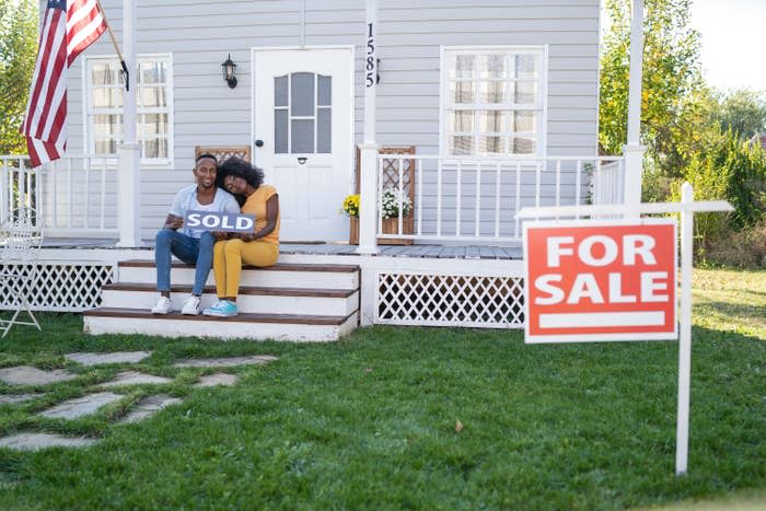 woman leans head on partner's shoulder as they sit on the porch of the house they just bought or sold