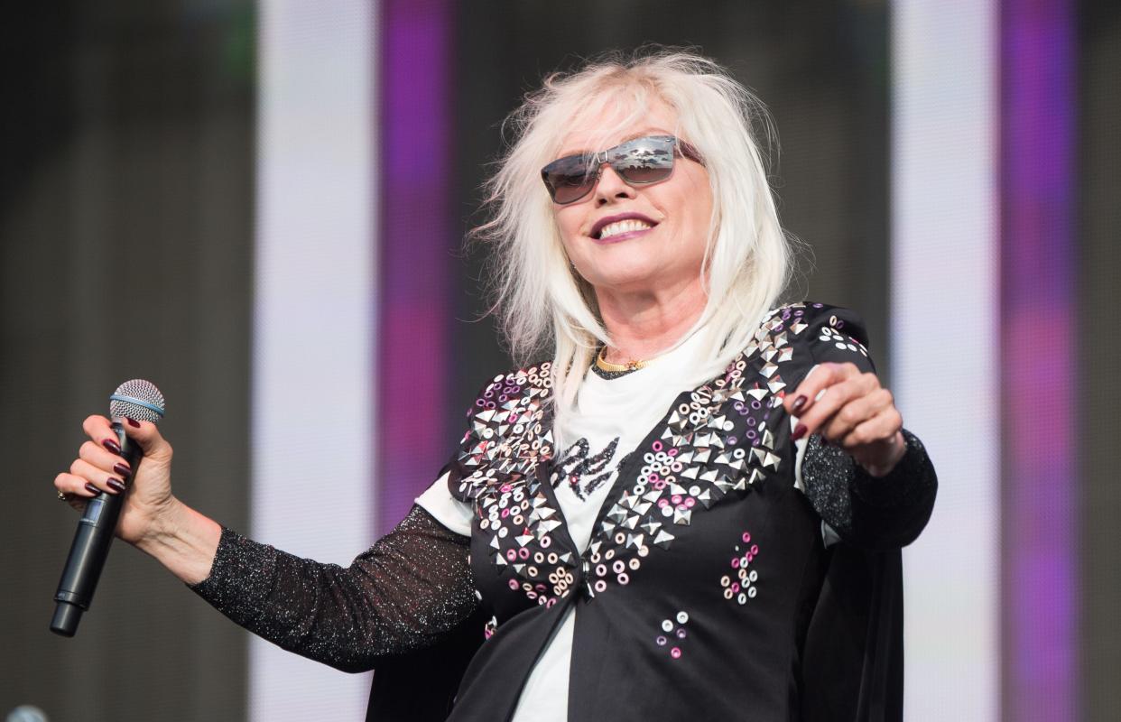 Debbie Harry of Blondie smiling and holding a microphone in a black jacket