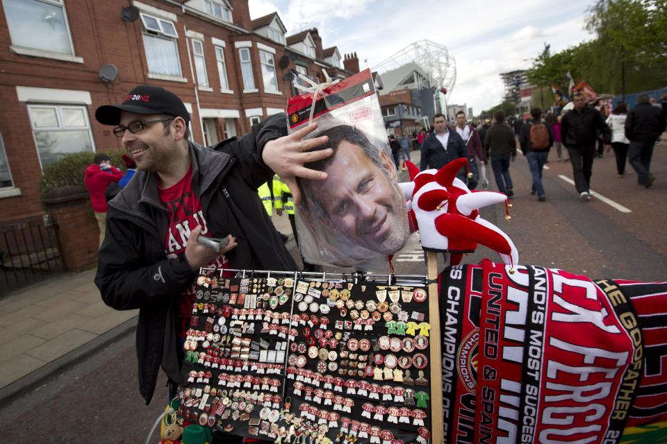 A merchandise seller stands alongside his stall featuring a mask of interim manager Ryan Giggs, centre, before Manchester United's English Premier League soccer match against Norwich City at Old Trafford Stadium, Manchester, England, Saturday April 26, 2014. (AP Photo/Jon Super)