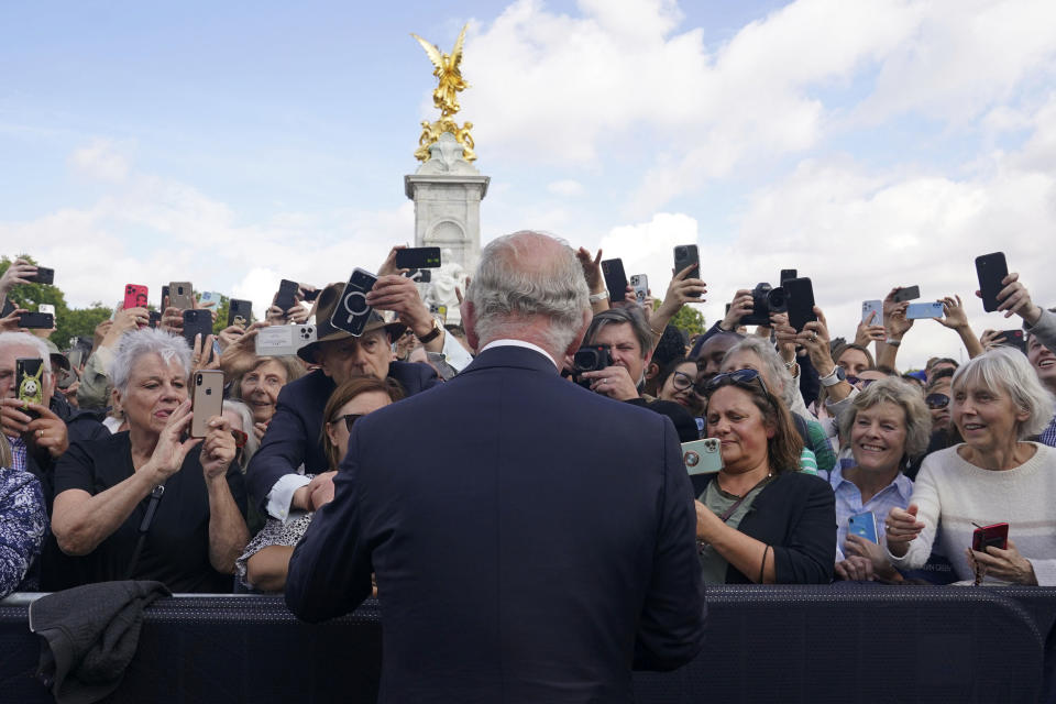 FILE - Britain's King Charles III, back to camera, greets well-wishers as he walks by the gates of Buckingham Palace following Thursday's death of Queen Elizabeth II, in London, Friday, Sept. 9, 2022. A year after the death of Queen Elizabeth II triggered questions about the future of the British monarchy, King Charles III’s reign has been marked more by continuity than transformation, by changes in style rather than substance. (Yui Mok/Pool Photo via AP, File)