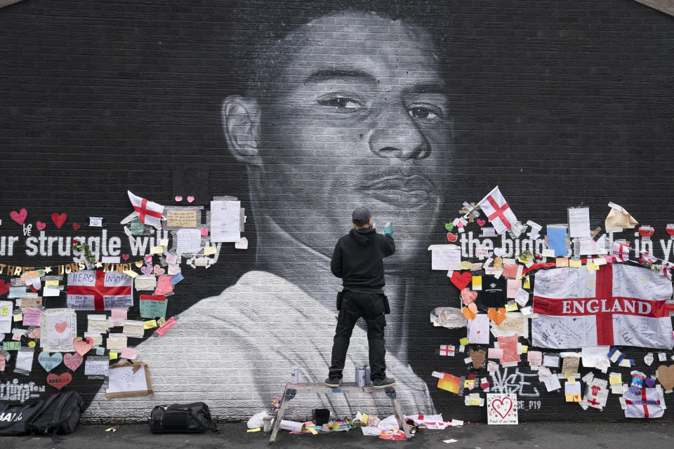 Street artist Akse P19 repairs the mural of Manchester United striker and England player Marcus Rashford on the wall of the Coffee House Cafe on Copson Street, in Withington, Manchester, England, Tuesday July 13, 2021. The mural was defaced with graffiti in the wake of England losing the Euro 2020 soccer championship final match to Italy, but subsequently covered with messages of support by well wishers. (AP Photo/Jon Super)