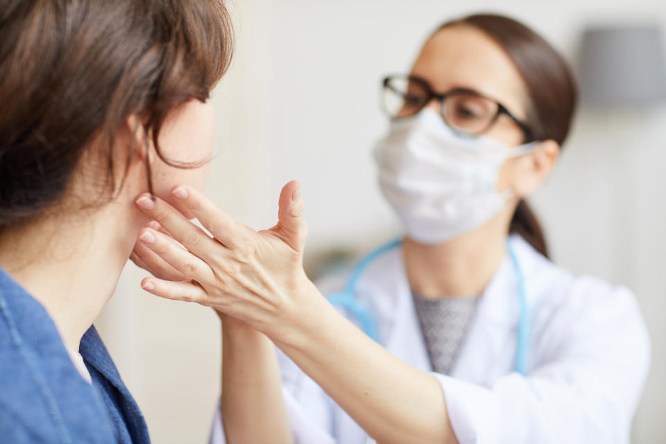 Young woman sitting while the nurse examining her throat during visit at hospital