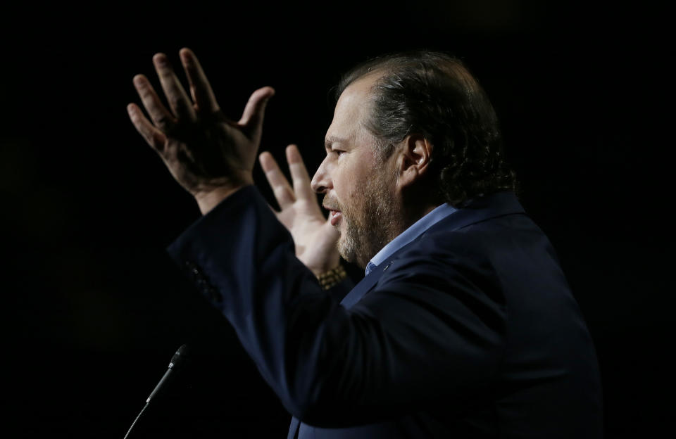 Salesforce CEO Marc Benioff speaks into a microphone against a dark background.