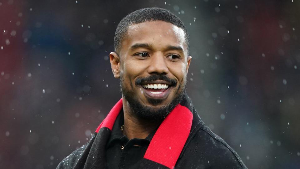 michael b jordan clapping and smiling while wearing a bournemouth scarf