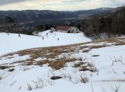 Grass sprouts through the snow as people enjoy skiing at a ski resort in Hakuba village