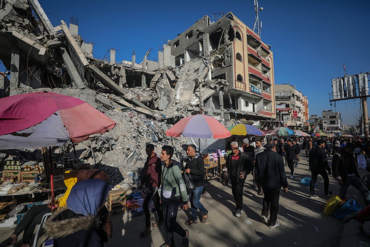 Palestinians walk past kiosks set up next to destroyed buildings along a street on the first day of Ramadan in Al Nusairat refugee camp in Gaza on 11 March (EPA)