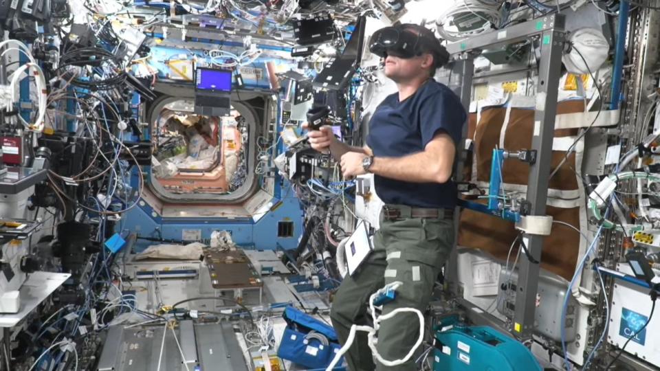     Ein Astronaut mit einem Virtual-Reality-Headset in einem überfüllten Raumstationsmodul. 