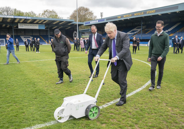 Prime Minister Boris Johnson paints over the white line of the centre circle during a visit to Bury FC at their ground in Gigg Lane, Bury, Greater Manchester. Picture date: Monday April 25, 2022.
