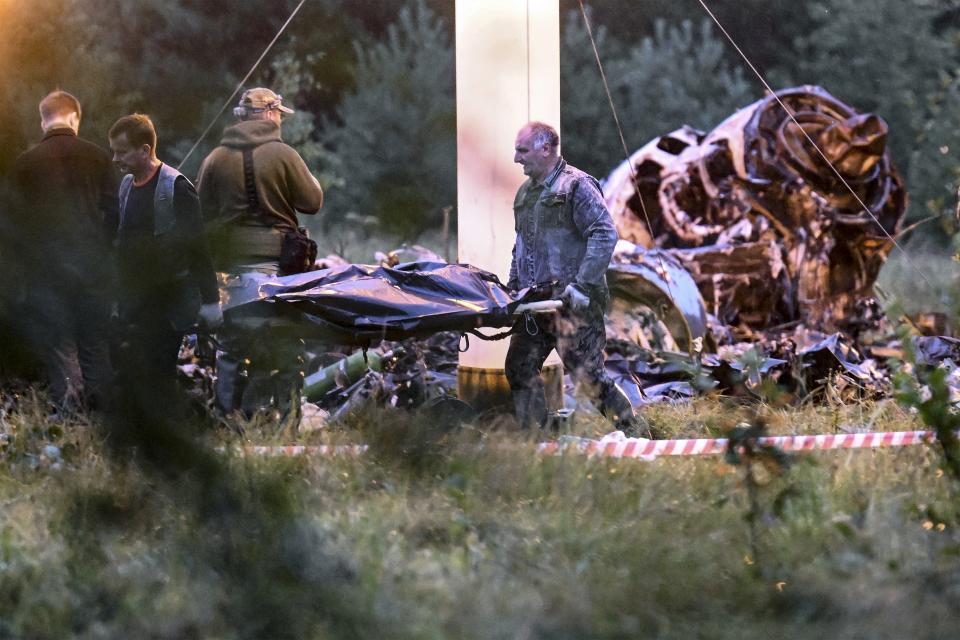 FILE - People carry a body bag away from the wreckage of a crashed private jet, near the village of Kuzhenkino, Tver region, Russia, on Aug. 24, 2023. Yevgeny Prigozhin dies exactly two months after the uprising in a mysterious plane crash. (AP Photo, File)