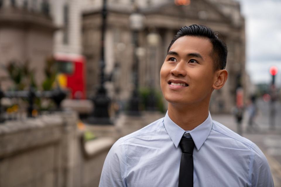 An investor standing on a city street smiles and looks upward.